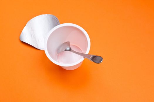 empty clean yogurt cup with spoon on an orange background