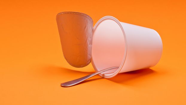 empty clean yogurt cup with spoon on an orange background