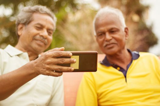 Selective focus on phone two Happy older men busy in watching mobile outdoor - concept of senior people using technology