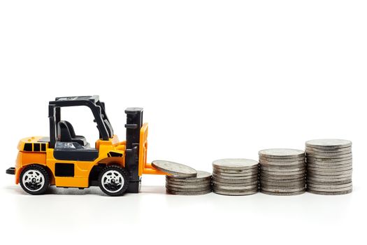 A yellow toy forklift with pile of coins on white background for saving money, investment, business and finance concept