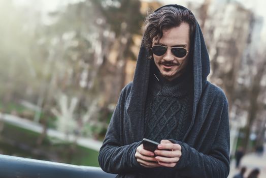 hooded stylish man in sunglasses walks In the park and texting message