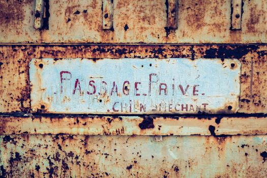 Private passage Bad dog written in French on a rusty metal barrier