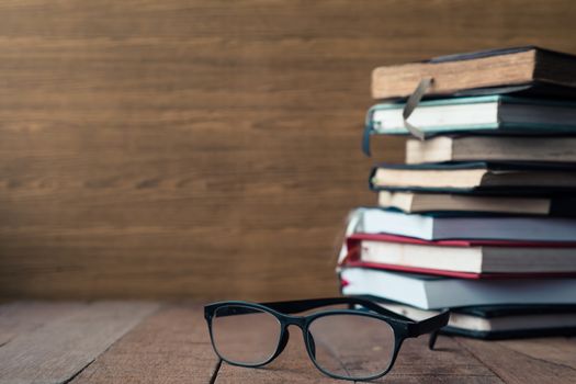 Glasses with hardback books on wooden table. Free space for text. Selective focus