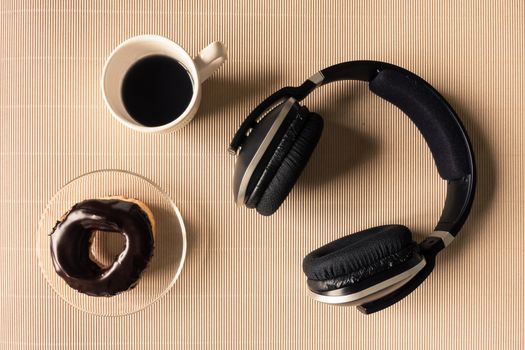 Top view of headphones with coffee cup and donut on table.