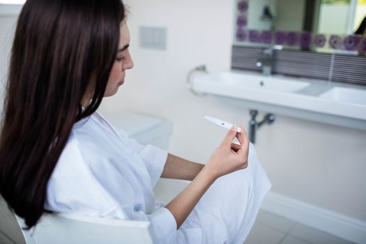 Unhappy woman sitting while looking at pregnancy test