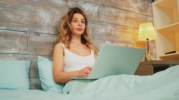Caucasian woman in pajamas reading an online article on her laptop