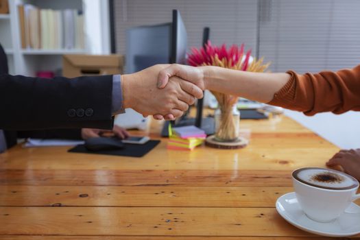 Businesspeople and partners shaking hands over the table, maintaining eye contact, confident entrepreneurs ready for effective negotiations, entering into a partnership, gender equality