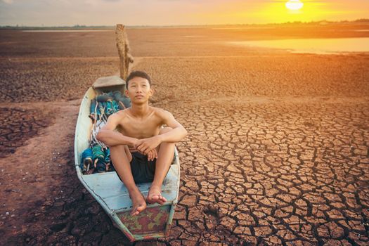 Sad a boy sitting on a boat that was parked in an arid ground fo