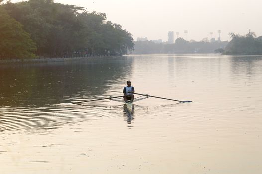 Individual Sports Speed Rower in Single scull crew rowing boat sliding racing shell on lake water oars in motion sitting sliding rigger seat doing exercise, fitness workout in sunset. Kolkata May 2019