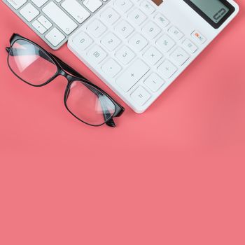 Top view female workplace, Computer keyboard, white calculator and glasses on a bright pink background.