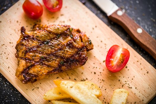 Grilled chicken steak on wooden cutting plate on black background.