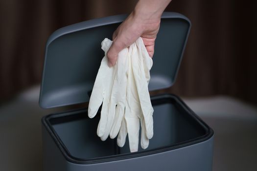 Hand putting used dirty surgical glove to  a garbage bin. Mask p