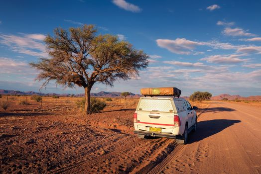 4x4 rental car equipped with a roof tent driving on a dirt road in Namibia