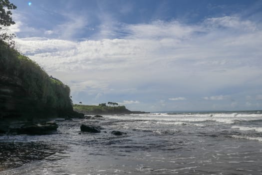 Indian Ocean coast near the Sacred Balinese temple Tanah Lot. Pura Batu Bolong on the edge of a cliff at coastline with hole in the rock. Holy place for local indonesian people