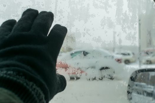 the hand of a man in a winter glove touches the icy glass of the car