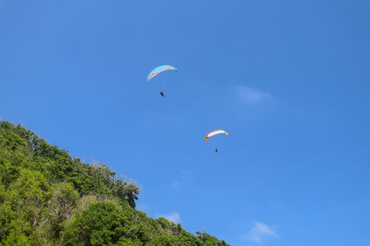 Paragliding in the sky. Two single paragliders flying in bright sunny day over tropical Bali island. Beautiful paraglider on a turquise background. Concept of active lifestyle and extreme sport.