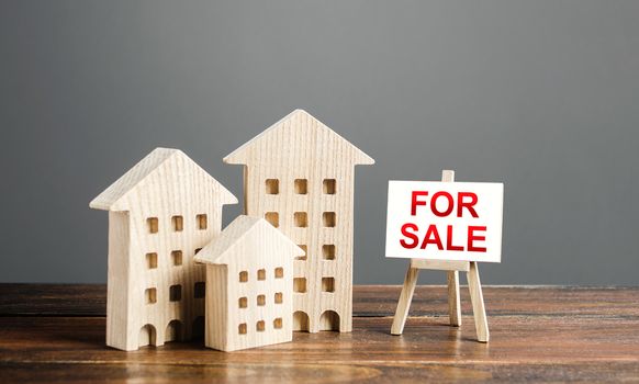 Wooden figures of residential buildings and an easel sign labeled for sale. Buying and selling real estate, hot offers and property valuation. Smart investments and relocation. Good offer