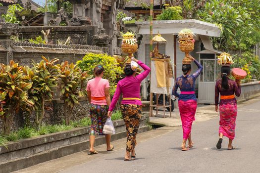Beautiful Balinese Women in Traditional Costumes - sarong, Carrying on Heads for ceremony. Women go to a Hindu temple. Arts festival, Bali island and Indonesia people culture. Asian travel background