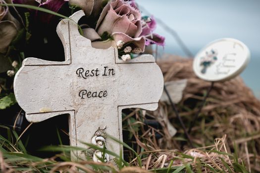 rest in peace written in English on a cross at the edge of a cliff