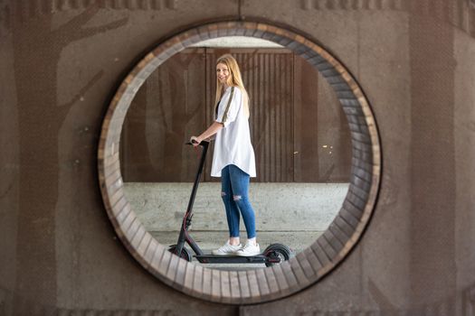 Casual caucasian teenager riding urban electric scooter in urban environment. Urban mobility concept