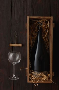 Bottle of red wine in wooden crate filled with straw next to to empty glasses with corkscrew on wooden table. Flat lay, above view, copy space,Chiaroscuro styled