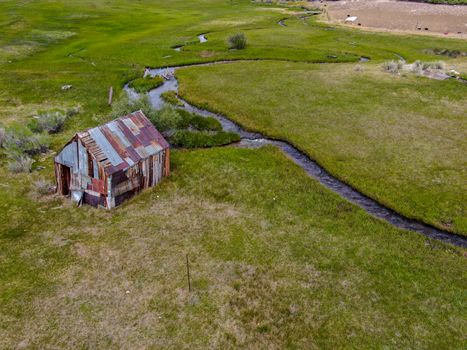 Aerial view of abandoned little wooden house barn next small river in the green valley, Aspen Spring