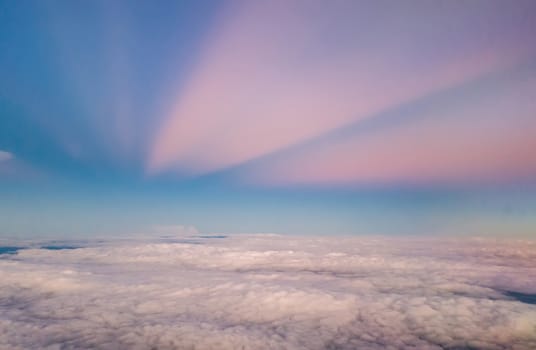 beautiful pastel sky atmosphere over white puffy cloud before sunset as seen through window of airplane, plane window. travel by airplane