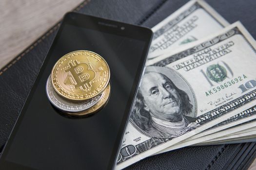 Golden bitcoins on the smart phone and us dollars with notebook on background. Bitcoin crypto currebcy. Digital currency. Profit from mining crypto currencies. Miner with dollars from trading.