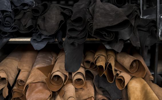 Different pieces of leather in a rolls. The pieces of the colored leathers. Rolls of natural brown and black and other leather. Raw materials for manufacture of bags, shoes, clothing and accessories.