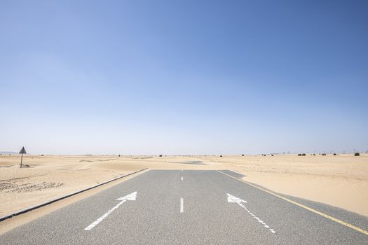 Horizontal shot of an empty road in the desert with large copy space in the blue sky