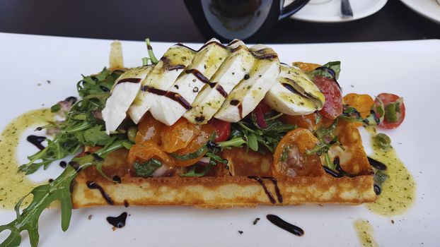 Mozzarella and arugula slices with tomatoes on a waffle. Drenched in balsamic sauce.