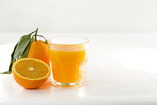 An inviting glass full of orange juice, a orange divided in two 