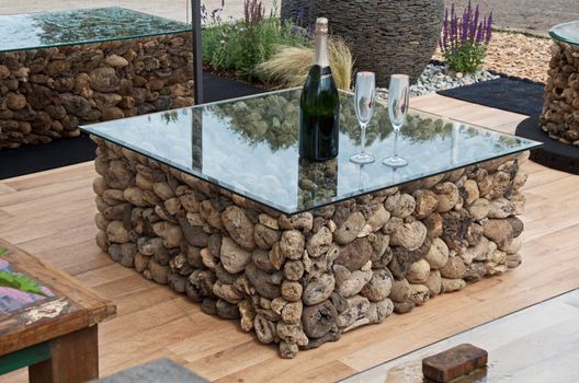 A coffee table made from driftwood with a modern glass top in a garden area