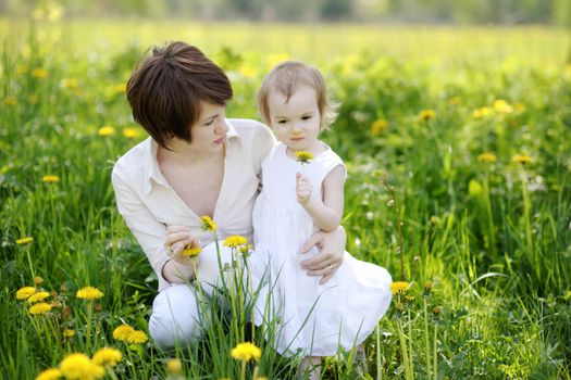 Youn mother and her girl in dandelions field