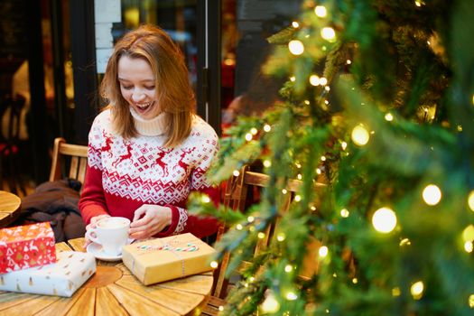 Girl in holiday sweater drinking coffee or hot chocolate in cafe decorated for Christmas