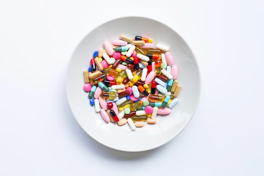 Colorful tablets with capsules and pills on white dish on white
