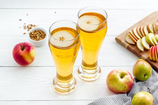 Glasses of beer with apple and peer on white wooden desk