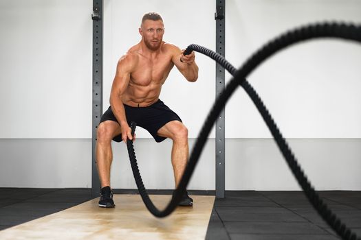 Gym battle rope man stamina training Athlete guy fitness exercising endurance indoor workout.