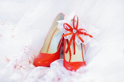 Elegant bright red bridal shoes and a white garter