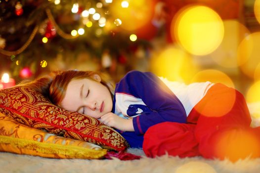 Adorable little girl sleeping under the Christmas tree by a fireplace on Christmas eve