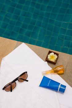 Sunglasses, bath towel, sunblock cream, bath gel and candle flower shape as spa set near the swimming pool