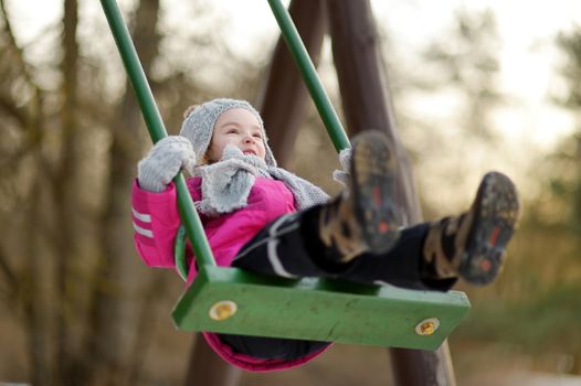 Adorable girl having fun on a swing on winter day