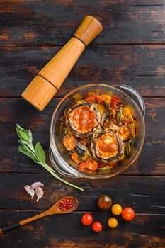 Portobello mushrooms,baked with cheddar cheese, cherry tomatoes and sage in glass pot on old wooden background top view.