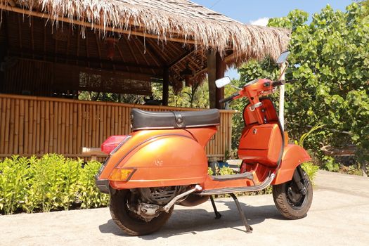 Classic scooter. Orange print Piaggio Vespa parked on a public street in Bali. Vintage scooter wheel and body design details. Indonesia, June 2019