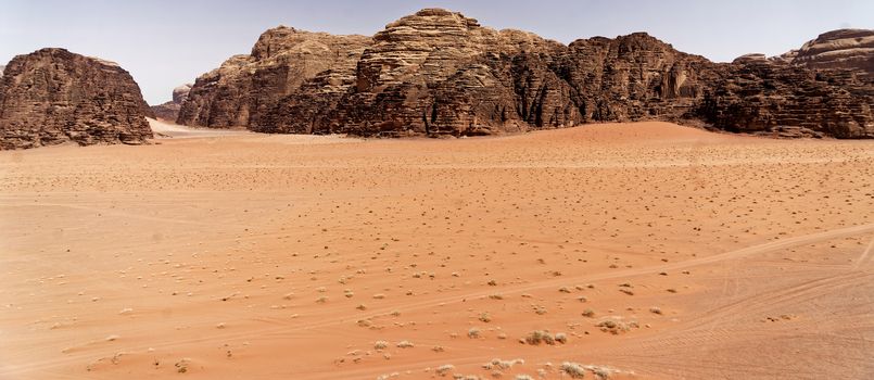 The emptiness of the great desert in the nature reserve of Wadi Rum, with large mountains of red sandstone in the background and the view over the wide sandy plain.