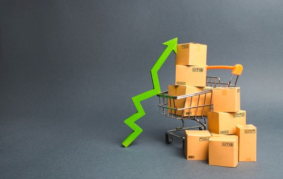 Shopping cart with cardboard boxes and a green up arrow. Increase the pace of sales and production of goods. Improving consumer sentiment, economic growth. Strategy for increasing revenue