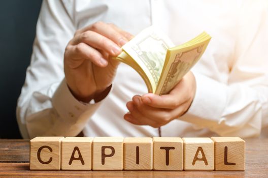 Businessman counts money on the background of the caption Capital. Capitalism, capital increase and influence. Financial liberalization of developing countries, unprincipled withdrawal of capital.