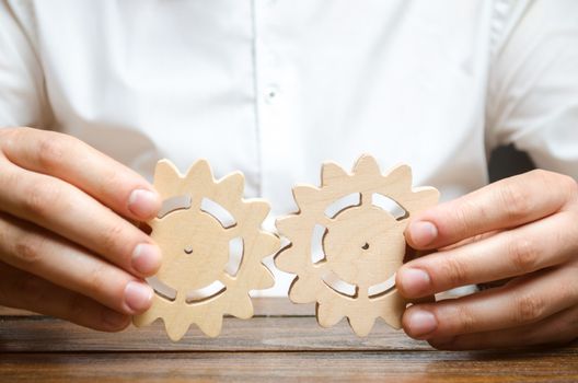 Businessman in white shirt connects two wooden gears. Symbolism of establishing business processes and communication. Improving work efficiency, establishing new connections and suppliers.