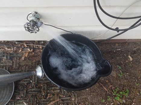 black plastic bucket being filled with water from a spigot