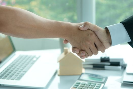 Estate agent sitting in a desk shaking hands with customers after signing a home purchase contract.